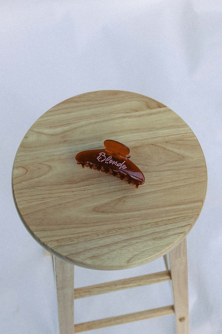 Small wooden stool with a brown hair clip sitting on top with a white background

